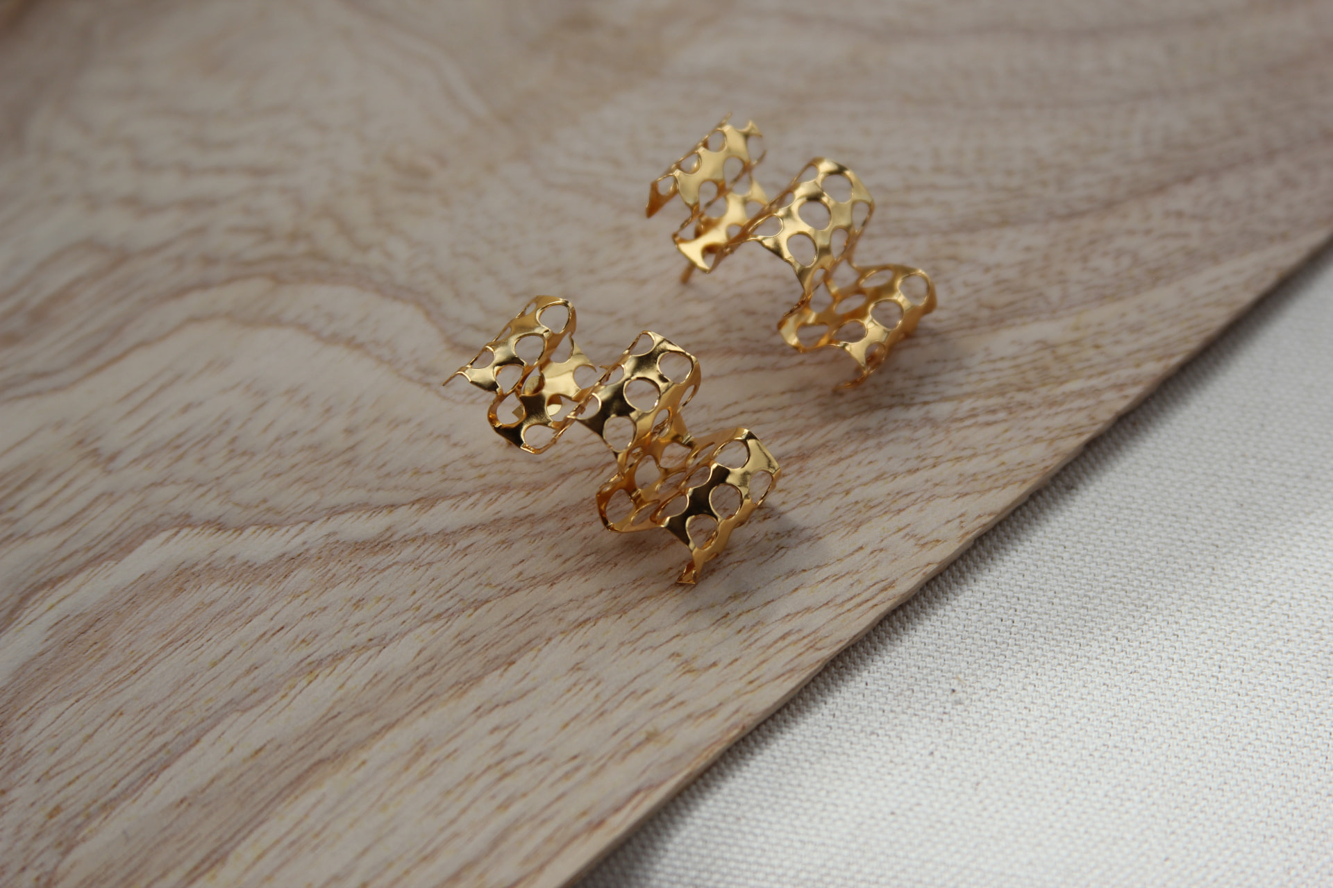 Aretes calados inspirados en el panal, en baño de oro, sobre madera clara