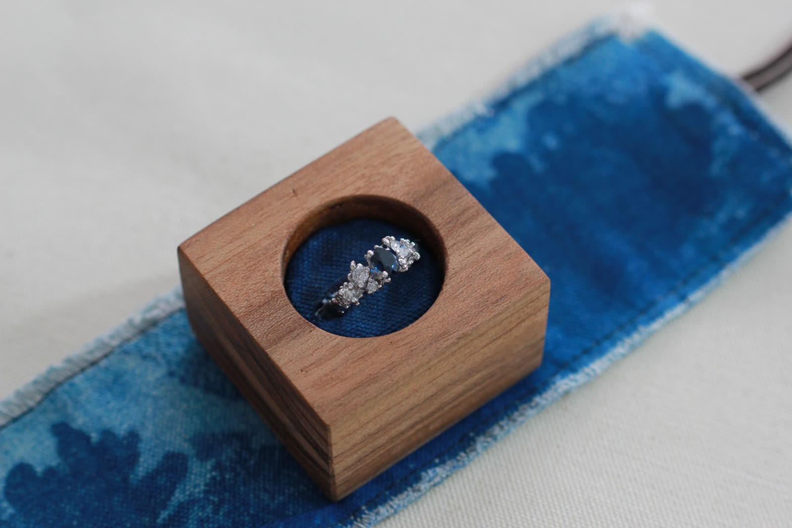 Anillo Tótem de Coral en oro blanco con zafiro central y diamantes, dentro de un cubo de madera sobre tela teñida en índigo